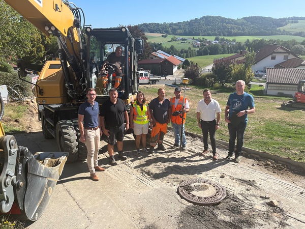 Die Verantwortlichen für die Baustelle stehen aufgereiht vor einem Bagger auf einer abgefrästen Straße.